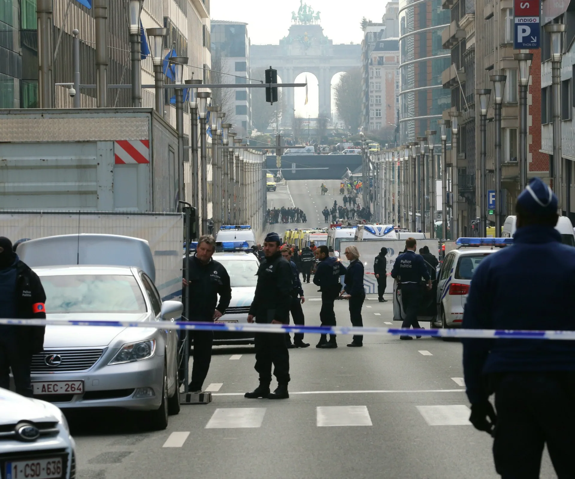 Police blockade in Brussels street, with emergency services vehicles and arch in the background.