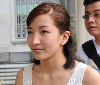 A woman with dark hair and light top walking outside, followed by a person in glasses.