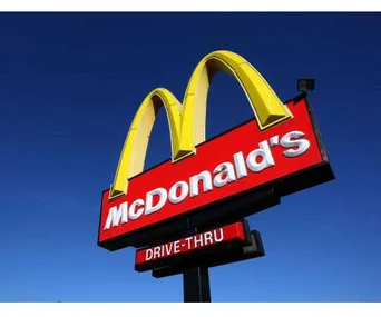 McDonald's drive-thru sign with iconic yellow arches set against a clear blue sky.