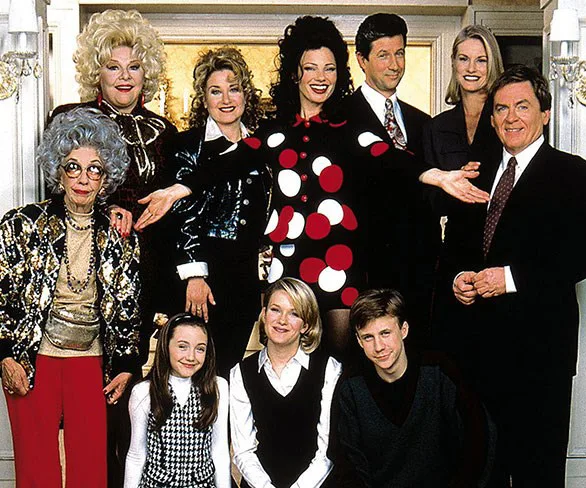 Cast of "The Nanny" in a group pose, featuring characters like Fran Fine, all smiling indoors in a formal setting.