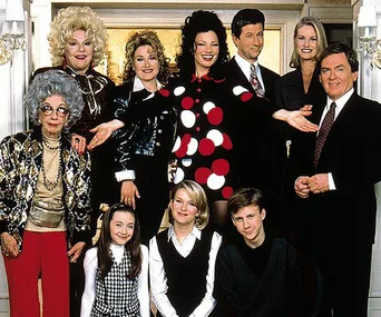 Cast of "The Nanny" in a group pose, featuring characters like Fran Fine, all smiling indoors in a formal setting.