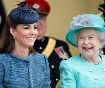 Two women smiling, wearing elegant hats and coats at a formal event, with a military officer in the background.