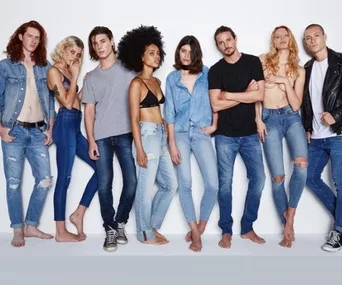 A group of diverse young adults posing in denim jeans and casual tops against a white background.