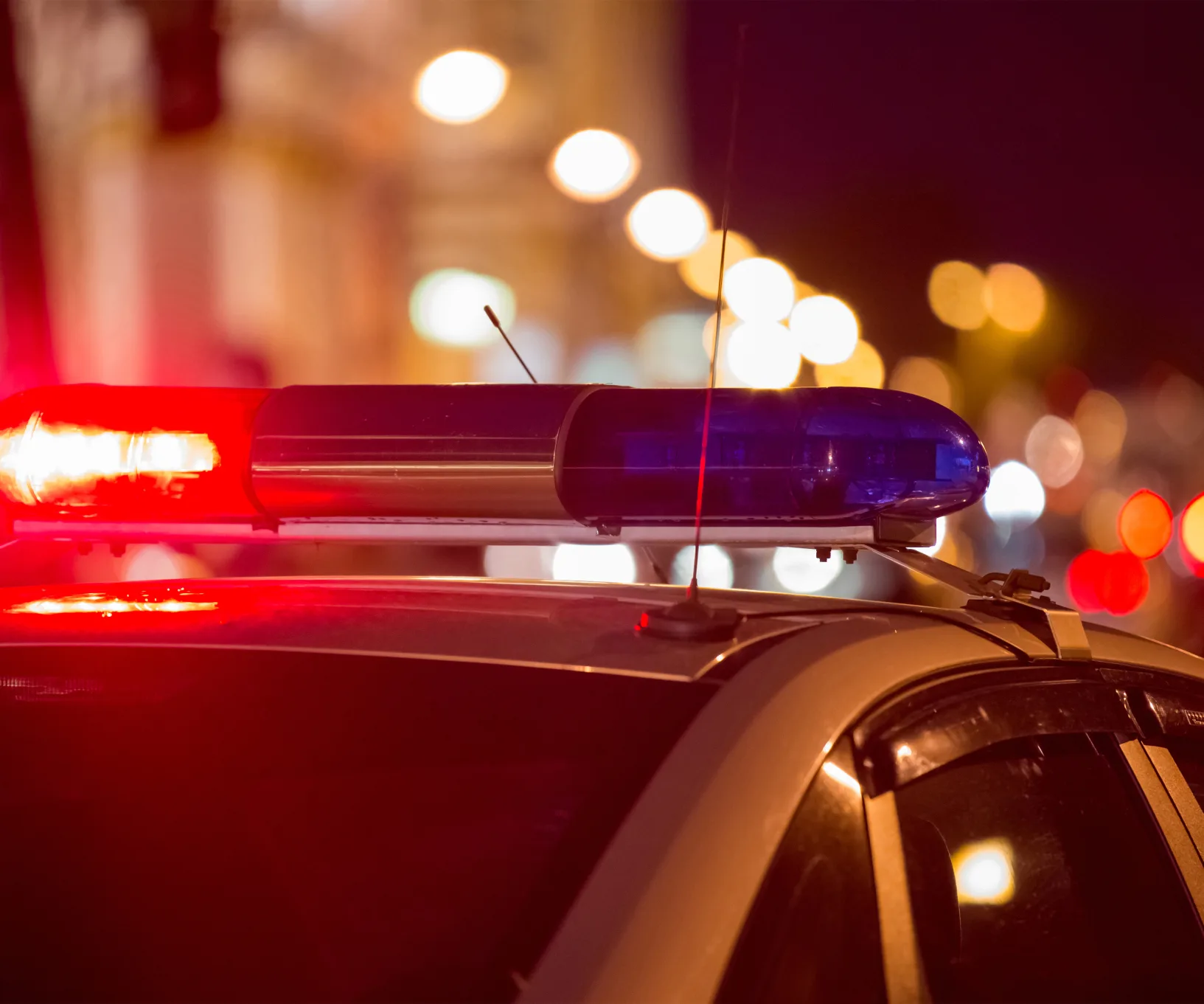 Police car with flashing lights at night, blurred city lights in the background.