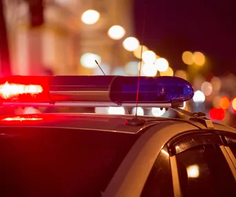 Police car with flashing lights at night, blurred city lights in the background.