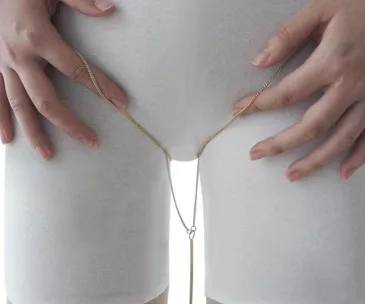 Thigh adorned with a delicate gold chain, highlighting space between legs against white fabric.