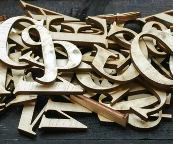 A pile of random wooden letters stacked on a dark surface.
