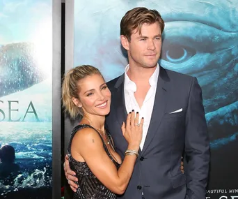 Couple posing at a movie premiere, close embrace, formal attire, blue ocean-themed background.