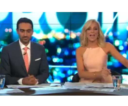 News anchors sitting at a desk, engaging with the camera in a brightly lit television studio.