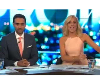 News anchors sitting at a desk, engaging with the camera in a brightly lit television studio.