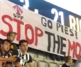 Banner at AFL game with “UPF Go Pies! STOP THE MOSQUE” behind fans, referring to anti-Muslim sentiment.