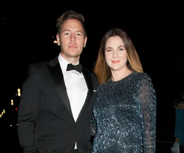 Drew Barrymore and Will Kopelman stand together, dressed elegantly, at a nighttime event.