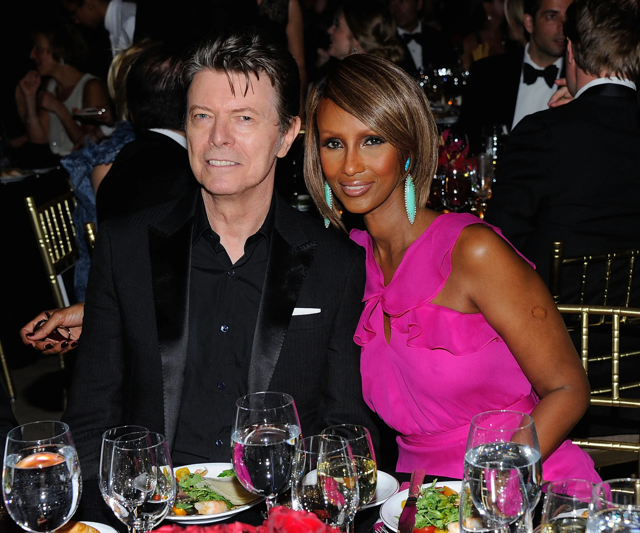 A couple sitting at a formal event, smiling, with a table set for dinner.