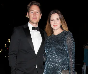 A man in a tuxedo and a woman in a sparkling dress smile at an event.