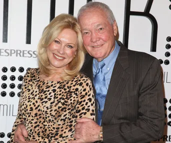 Couple smiling together; woman in leopard print dress, man in suit with blue tie, posing at an event backdrop.