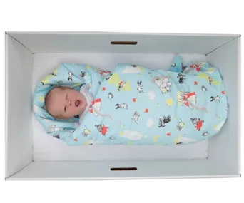 Baby wrapped in a colorful blanket, sleeping in a cardboard box crib.