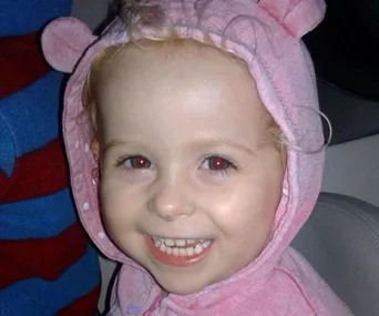 A smiling toddler in a pink hoodie with bear ears.