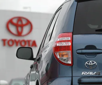 Rear view of a blue Toyota RAV4 with logo, parked outside a Toyota dealership.