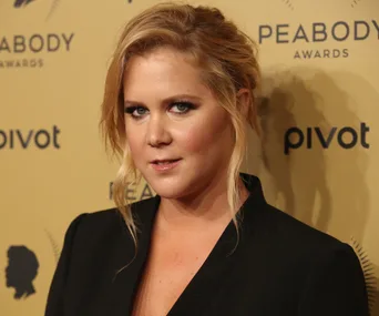 Comedian at the Peabody Awards, posing on a gold backdrop with a Peabody silhouette and logos in the background.