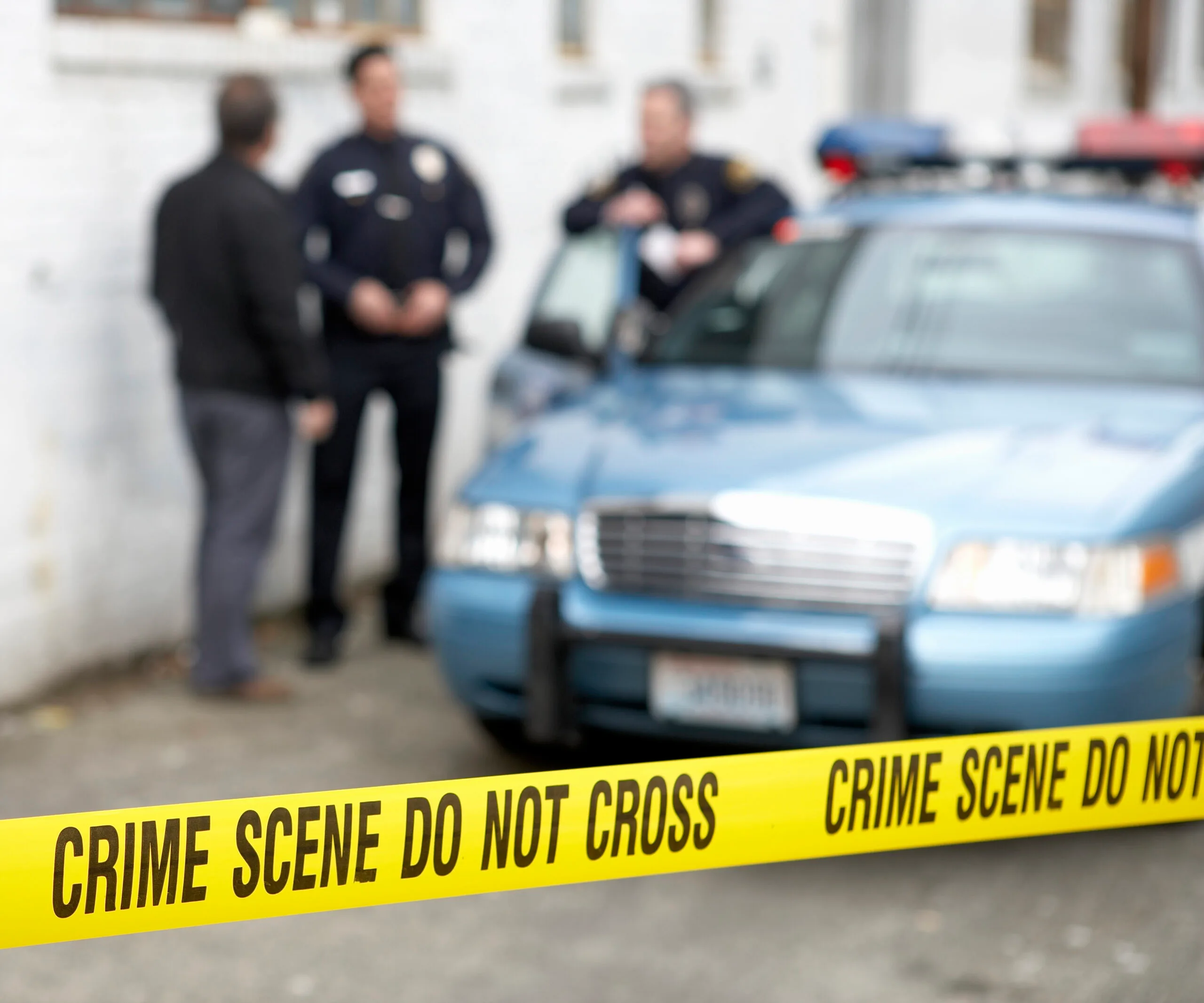 Blurred scene with police officers by a car behind crime scene tape.