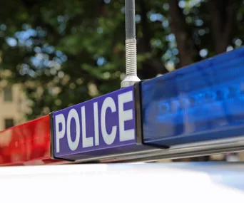 Police vehicle light bar with red and blue lights against blurred trees background.