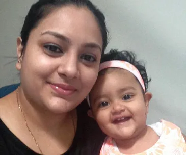 A woman smiling next to a smiling baby in a headband.