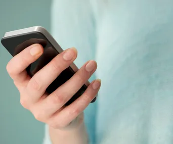 Person holding a smartphone in their hand against a blurred blue background.