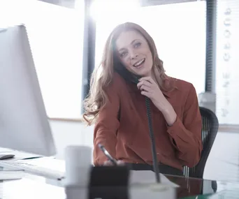 Woman in an office smiling while talking on the phone and writing notes.