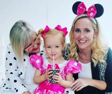 Woman in Minnie Mouse ears, child in costume sipping from a straw, with another woman in polka dots smiling at them.