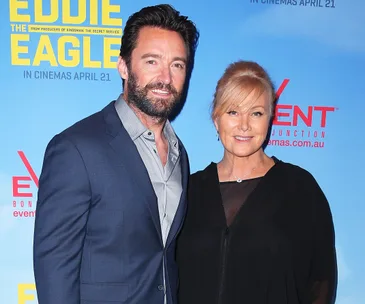 A couple poses at an "Eddie the Eagle" movie event, standing in front of a promotional backdrop.