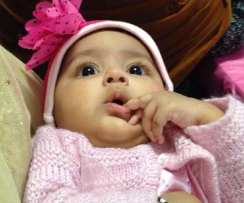 Toddler in pink knitwear and hat with a pink bow, looking up with a curious expression.