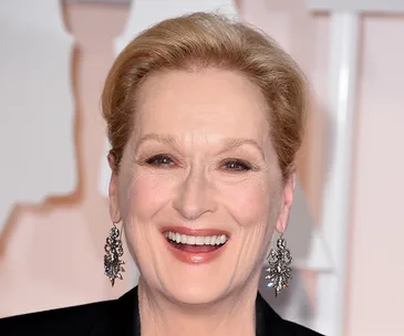 Meryl Streep smiling at a formal event, wearing ornate earrings and a black outfit.