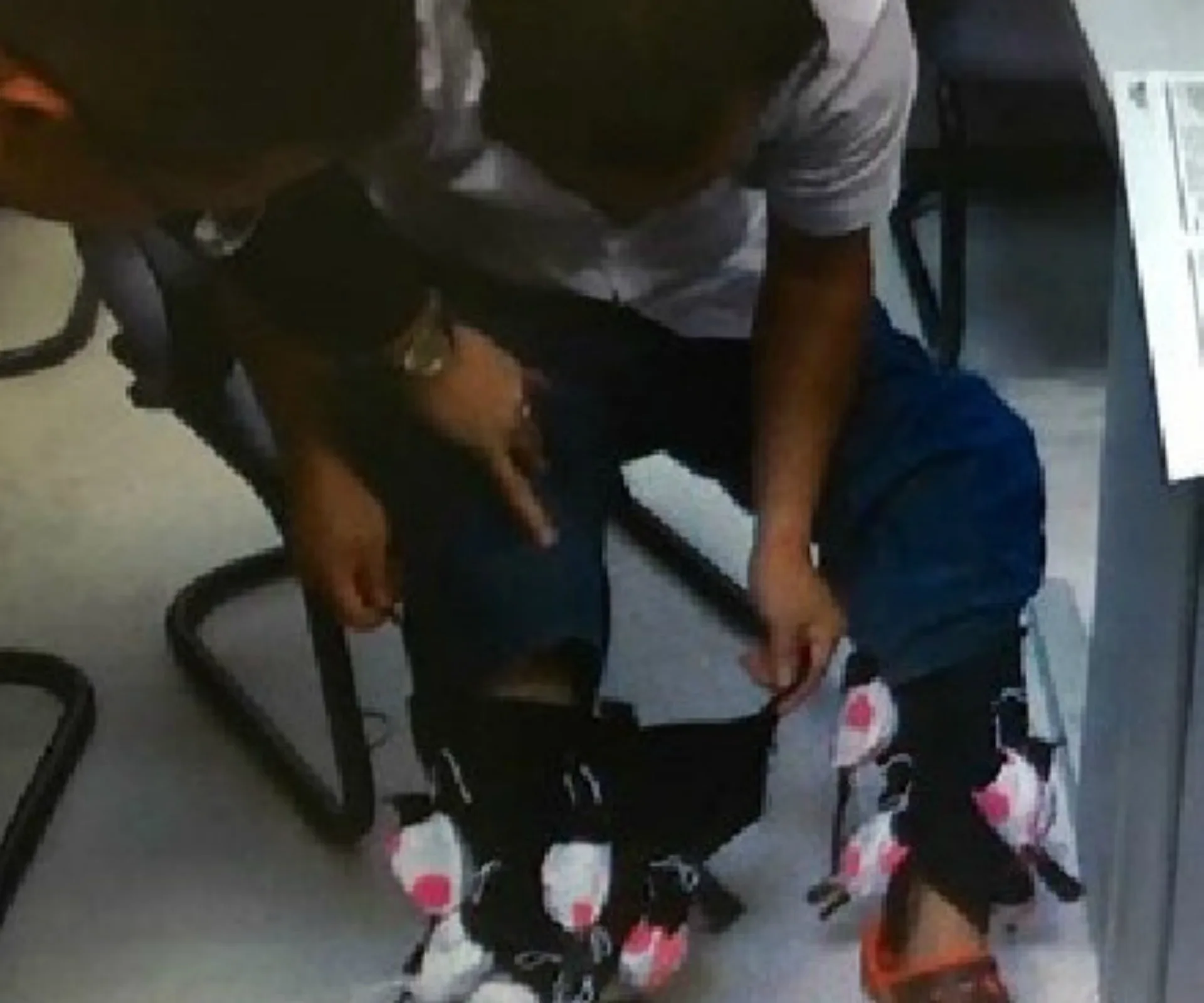 A man is sitting, showing live exotic birds tied around his legs under pants.