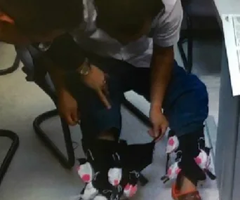 A man is sitting, showing live exotic birds tied around his legs under pants.