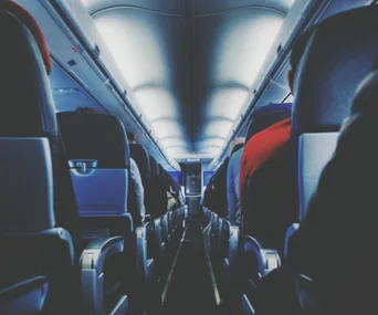 Airplane cabin interior from aisle perspective, with rows of occupied seats and overhead compartments.