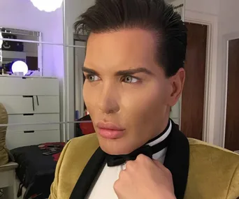A person with styled hair and a bow tie, looking sideways in a room with mirrored furniture.