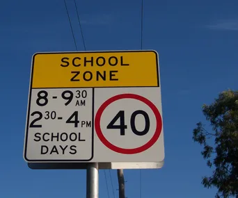 School zone sign indicating 40 km/h speed limit during specific hours on school days, with a clear blue sky background.
