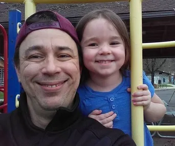 Father and daughter smiling together at a playground, showing a joyful reunion moment.