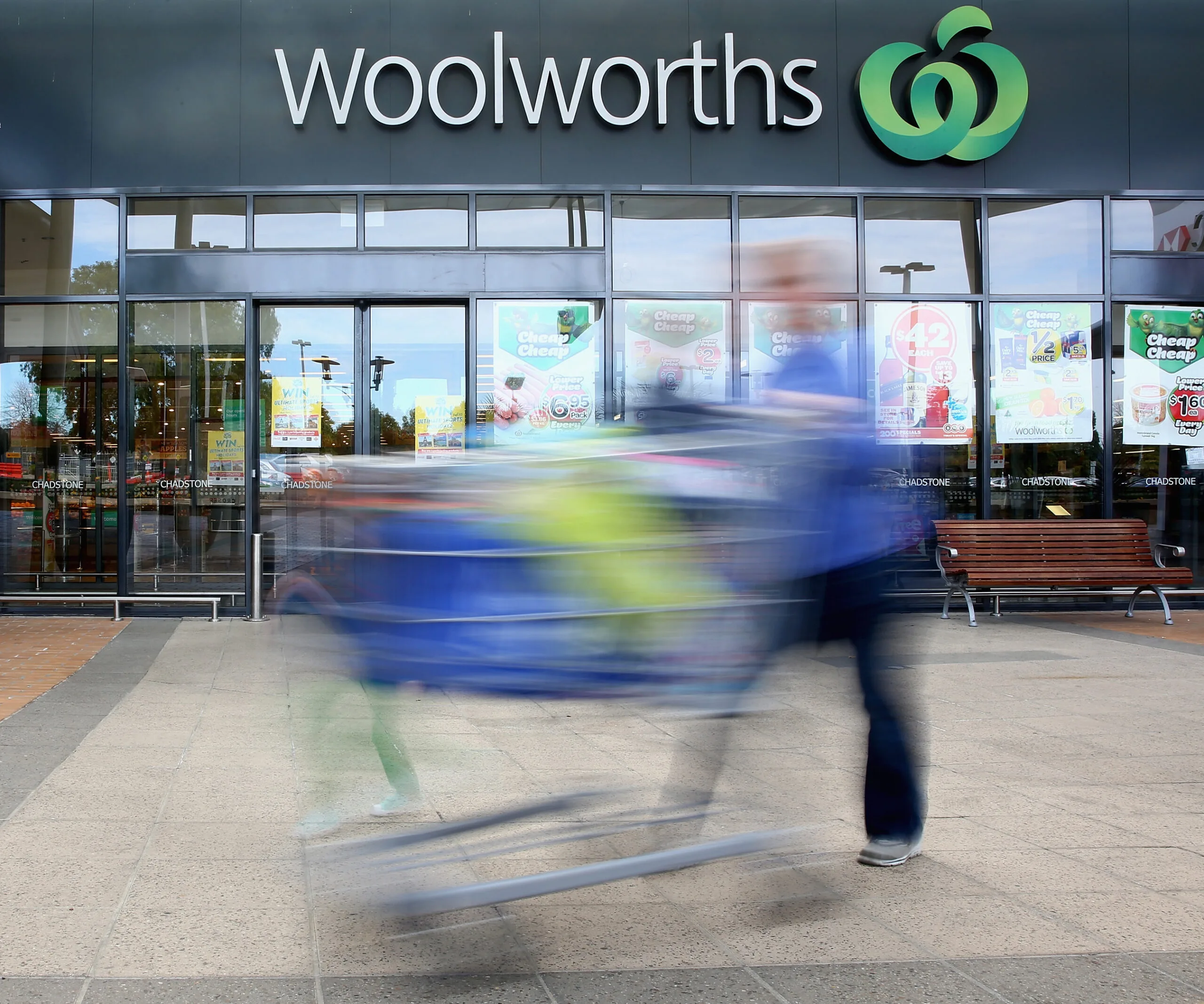A person pushing a shopping cart quickly in front of a Woolworths storefront.