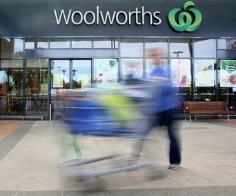 A person pushing a shopping cart quickly in front of a Woolworths storefront.