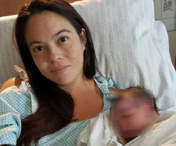 Mother in hospital gown holding newborn, both in bed.