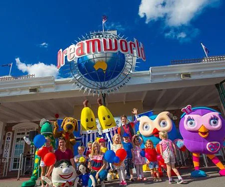 Group of children and mascots in colorful costumes posing at the entrance of Dreamworld amusement park under a sunny sky.