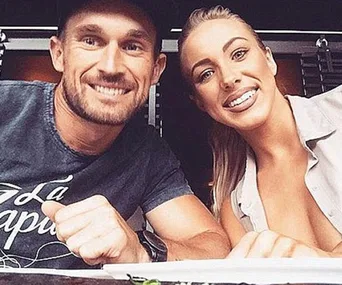 A smiling man and woman sitting together, looking at the camera in a casual setting.