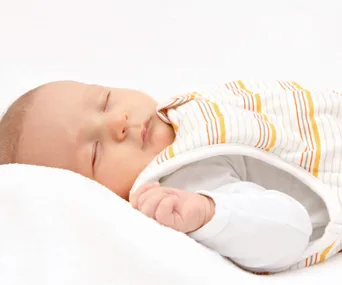 A baby peacefully sleeping in a striped sleeping bag on a white background.