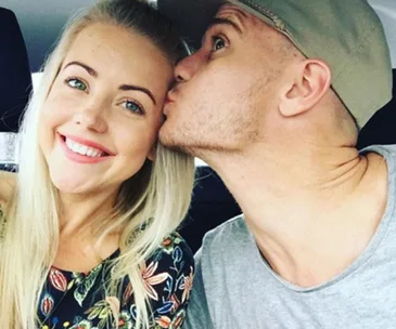 Couple in car, woman smiling, man in cap kissing her cheek lovingly.