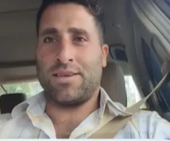A person sitting in a car, wearing a seatbelt, looking at the camera during the daytime.