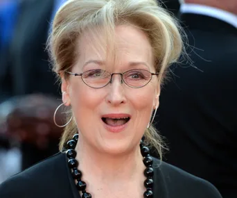 Meryl Streep at a red carpet event, looking surprised, wearing glasses and a black necklace.