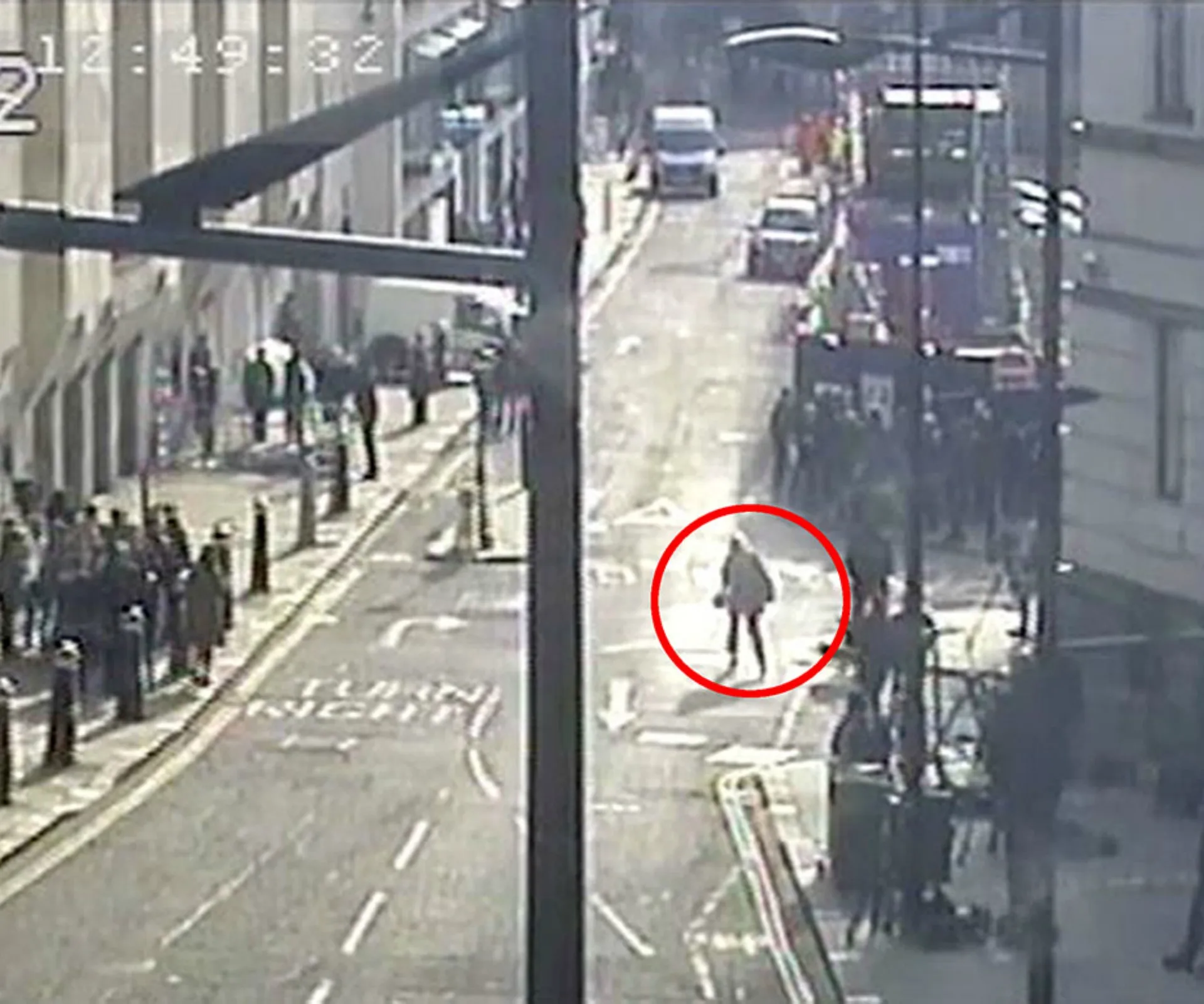 CCTV footage of a street with a person circled in red, indicating focus on their actions or movement.