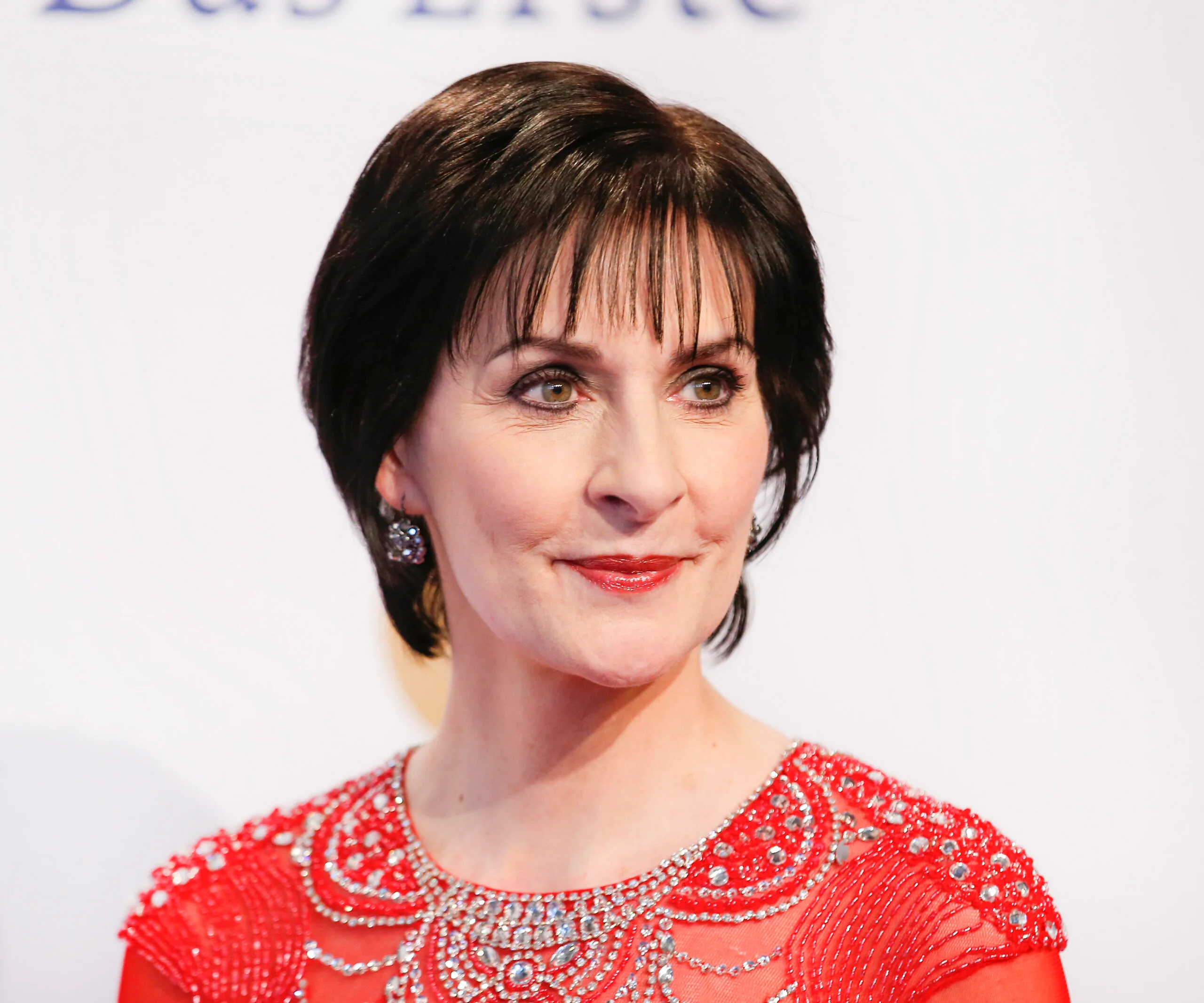 Enya in an elegant red dress adorned with intricate beading at an event.