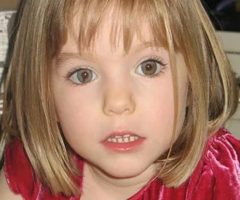 A young child with short blonde hair, wearing a red dress, looking directly at the camera.